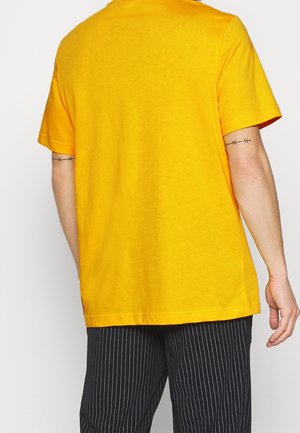 T-shirt en coton jaune à manches courtes et col rond. Texture lisse et coupe décontractée, associé à un pantalon noir à rayures fines.