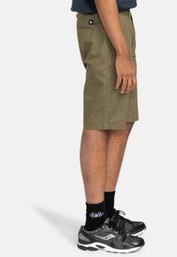 Olivgrön shorts i bomull med en platt framdesign och sidofickor. Matchas med svarta sneakers och strumpor. Sido vy.