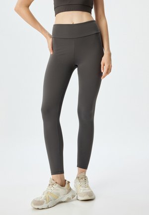 Donkergrijze leggings met een hoge tailleband, een gladde textuur en een aansluitend ontwerp, gecombineerd met lichtgekleurde sportschoenen.