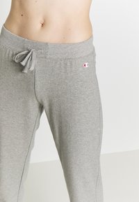 Gray sweatpants made of soft fabric, featuring a drawstring waistband and a small logo on the left side. Relaxed fit and smooth texture.