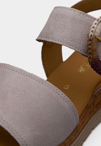 Ανοιχτό γκρι σουέντ σανδάλι με φαρδιά λουρίδα, πλεκτή διακόσμηση και επίπεδη σόλα εσπαντρίγιας. Διαθέτει εμφανείς ραφές και λείο εσωτερικό επένδυση.