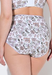Des sous-vêtements floraux taille haute en blanc avec des motifs violets, verts et marron. Ils présentent une texture douce et une délicate bordure en dentelle le long de la taille.