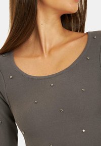 Szary długi rękaw top z dekoltem w serek, z prążkowaną teksturą i rozproszonymi metalicznymi zdobieniami na tkaninie.