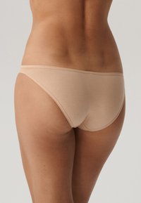 Beżowe majtki o gładkiej teksturze, niskim kroju i minimalnym zakryciu. Wyposażone w cienką talię i bezszwowe krawędzie. Idealne do codziennego noszenia.