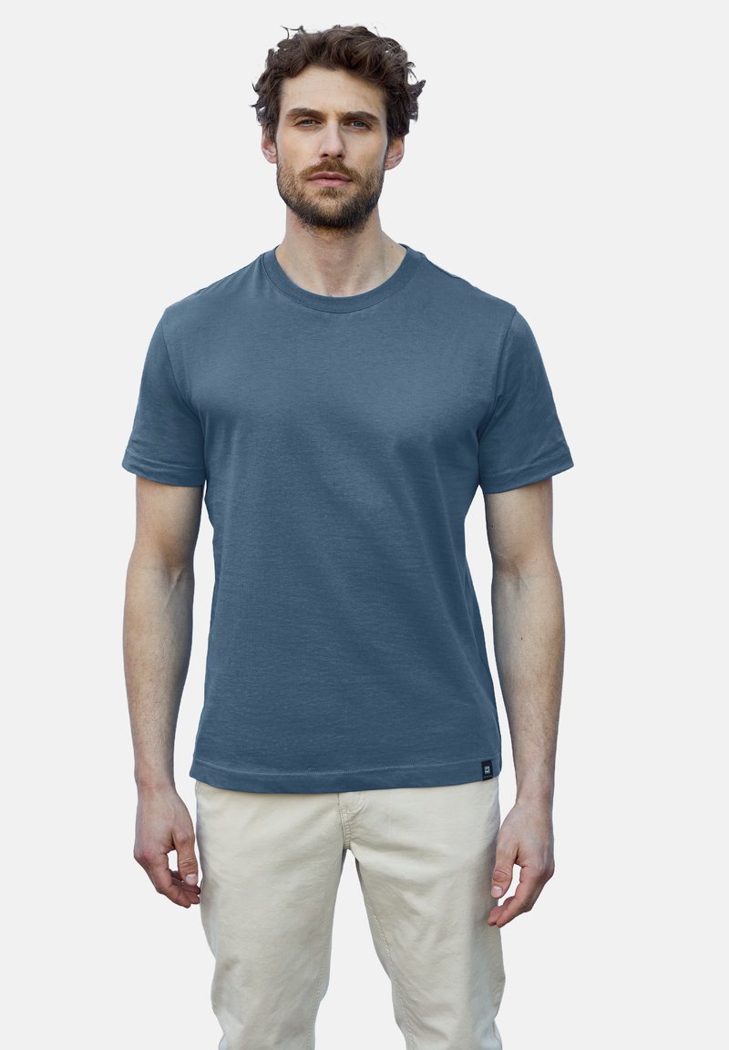 Pánské tričko s kulatým výstřihem v tmavě modré barvě, vyrobené z texturované látky, s krátkými rukávy a slim fit střihem. Bílé kalhoty.