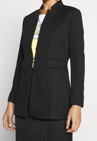 Svart blazer med strukturerad yta, enkelknappstängning och två framfickor. Har en smal passform och design med klippt krage.