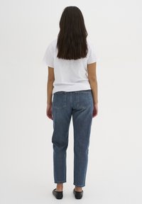 Jeans in denim blu con vestibilità dritta, dotati di due tasche posteriori, abbinati a una semplice t-shirt bianca di cotone, visti dal retro.