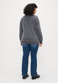 Pulôver cinza com um corte descontraído, punhos e bainha canelados, combinado com jeans azul de perna reta e sapatos escuros.