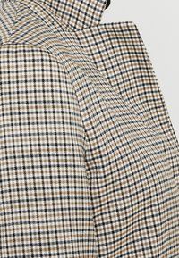 Tkanina s textura a károvaným vzorem v černé, bílé a hnědé barvě. Materiál vypadá tkaný a strukturovaný.