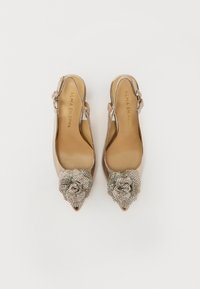 Zapatos slingback de punta afilada en un beige metálico, con un adorno de tela texturizada en forma de flor embellecida con rhinestones plateados.