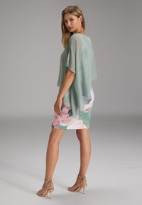 Abito con motivo floreale e sovrapposizione trasparente verde menta. L'abito presenta maniche corte, un design aderente e una morbida texture del tessuto. Tacchi dorati.