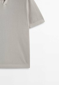 Haut à manches courtes rayé gris clair avec un décolleté en V. Tissu texturé avec de légères lignes horizontales. Présente une silhouette décontractée et carrée.