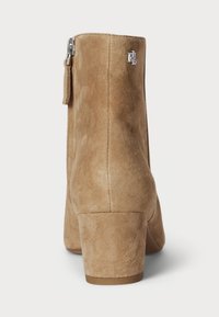 Bottine en suede tan avec un talon bloc, fermeture éclair et un accent logo. Présente une texture lisse et un design épuré.