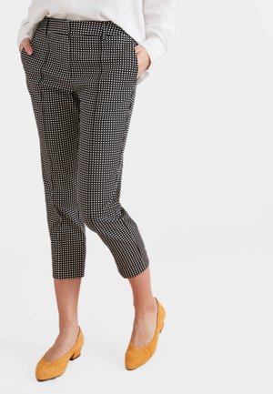 Pantalons cropped à pois noirs et blancs avec poches latérales, coupe ajustée et texture de tissu lisse, associés à des chaussures de couleur moutarde.
