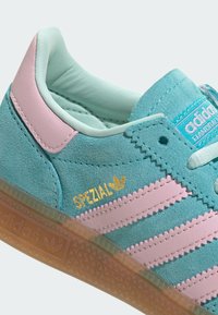 Zapatilla Adidas de ante en color verde azulado con rayas rosa pastel, lengüeta rosa en el talón, suela de goma y logo dorado "SPEZIAL" en el lateral.
