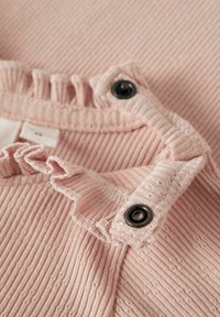 Primer plano de una tela ribeteada rosa con bordes rizados y dos botones a presión negros en una prenda.