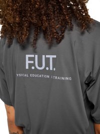 Person with curly hair wearing a dark gray shirt with white text "F.U.T. Physical Education & Training" on the back.