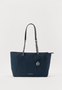 Sac fourre-tout marine en matériau lisse, avec des poignées en chaîne et en cuir, un pendentif logo rond et un nom de marque en relief subtil.