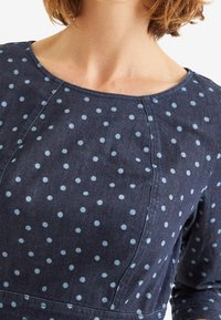 Dunkelblaues Denimkleid mit hellblauen Punkten. Es hat einen runden Ausschnitt und lange Ärmel, zeichnet sich durch eine glatte Textur und eine taillierte Passform aus.