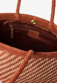 Sac fourre-tout tissé marron et beige avec des poignées tressées, ouverture sur le dessus révélant un intérieur en tissu marron avec une poche zippée et une fermeture à pression magnétique.