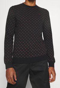 Black sweatshirt with a textured surface, featuring a small red floral pattern, ribbed cuffs, and hem. Crew neckline and fitted silhouette.