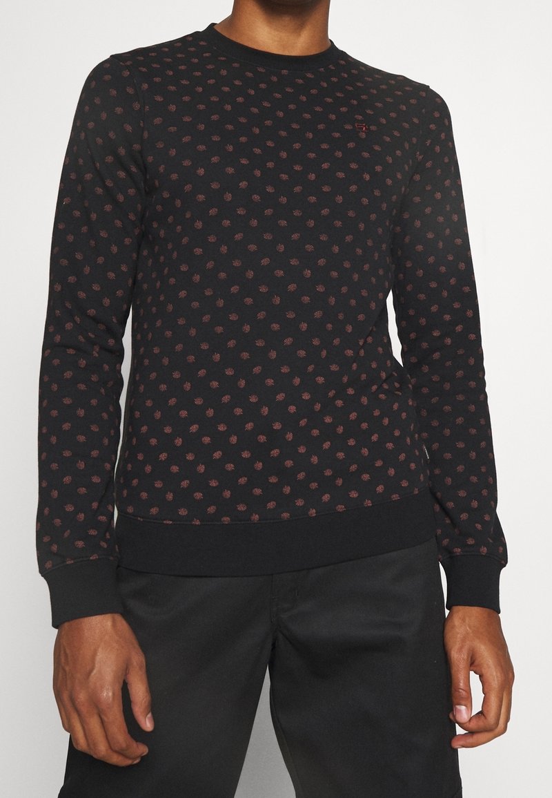 Black sweatshirt with a textured surface, featuring a small red floral pattern, ribbed cuffs, and hem. Crew neckline and fitted silhouette.