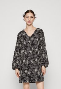 Robe noire avec un décolleté en V et de longues manches bouffantes, arborant un motif floral blanc et une coupe ample, réalisée dans un tissu léger.