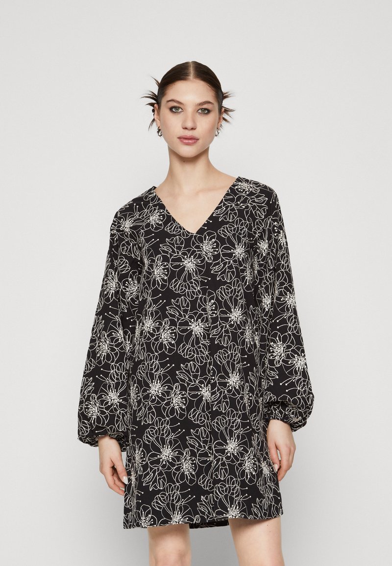 Robe noire avec un décolleté en V et de longues manches bouffantes, arborant un motif floral blanc et une coupe ample, réalisée dans un tissu léger.