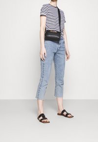 Bolso cruzado negro con herrajes dorados, blusa de rayas de manga corta, jeans cortos azul claro, y sandalias planas negras con tiras anchas.
