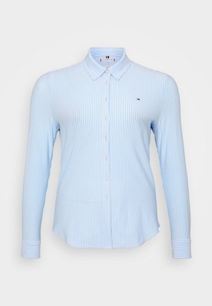 Lys blå langermet skjorte med vertikale hvite striper, knappelukking, klassisk krage og en liten logo på brystet.