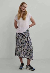 Fehér, rövid ujjú felső, amelyhez fekete virágmintás maxi szoknya van párosítva, pasztell virágokkal. Fekete sportcipővel viselve, kék részletekkel.