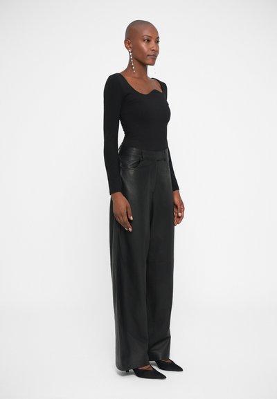 Top negro de manga larga con escote corazón, combinado con pantalones de cuero negros holgados y zapatos negros de punta. Pendientes plateados sencillos.