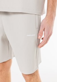 Gray ribbed shorts with a side pocket and white "PEGADOR" logo. The fabric has a soft texture and a straight hem design.