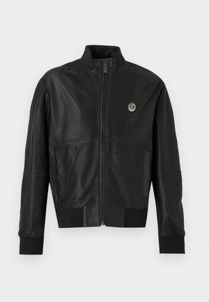 Mustast nahast auguline jakk esikinnise, kõrge kaeluse, soonikkoes mansettide, taskute ja vasakul rinnal asuva väikese ümmarguse logoga.