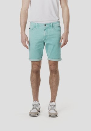 Lyse turkise denimshorts med op rullede kanter, fem lommer og diskret falmet effekt. Bæres med en hvid t-shirt og lyse sneakers.