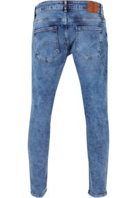Jeans de denim azul slim fit con un lavado desgastado, cinco bolsillos y una parche de cuero marrón en la cinturilla. Textura suave, longitud estándar.