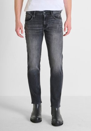 Donkergrijze slim-fit jeans in een vervaagde wassingen, met vijf zakken, zichtbare stiksels en een sluiting met een knoop aan de voorkant. G gedragen met zwarte enkellaarsjes.