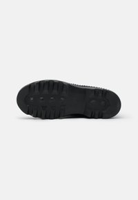 Suela de zapato negra con profundas huellas, patrones hexagonales y costillas texturizadas. Hecha de goma duradera para ofrecer tracción en diversas superficies.