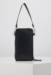 Mustalla nahkalompakolla, jossa on pystysuuntainen muotoilu. Lompakossa on sivuvetoketju ja irrotettava hihna, ja sen pinnassa on sileä rakenne sekä minimaalinen varustus.