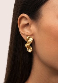 Pendientes de oro con tres piezas redondeadas y texturizadas, que exhiben un acabado brillante y suaves surcos. Diseñados para ser usados en la oreja.