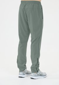 Groene, lichte sportbroek met een elastische tailleband, zijzakken met rits en een slim fit, gecombineerd met grijze hardloopschoenen.