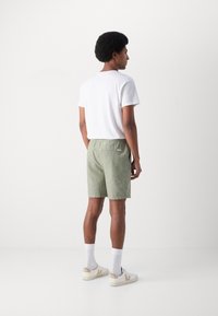 Lichtgroene shorts van een textuurstof, met een elastische tailleband en een achterzak. Gecombineerd met een wit t-shirt en witte sneakers.