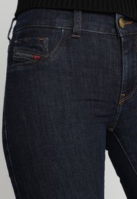 Jeans de mezclilla azul oscuro con un corte slim, que cuentan con costuras en naranja contrastante, un pequeño bolsillo trasero y un cierre de botón metálico.