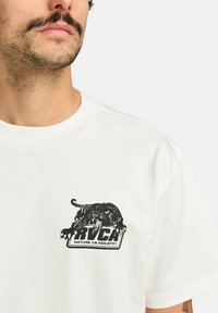 Witte katoenen t-shirt met een zwarte grafiek van een panter en de tekst "RVCA NATURE VS INDUSTRY" op de linkerkant van de borst.