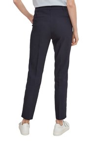 Námořnické modré kalhoty na míru se slim fit střihem, s polovičním pasem, zadními kapsami a hladkou texturou, doplněné bíl�ými teniskami.