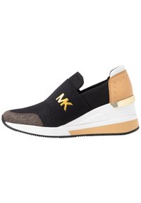 Baskets noires à enfiler avec un bout marron, une semelle compensée beige et blanche, des clous dorés sur le talon et un logo "MK" doré sur la bande élastique devant.