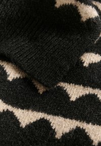 Tessuto di lana lavorato a maglia caratterizzato da un motivo zigzag nero e beige. La texture appare morbida con una finitura leggermente pelosa.