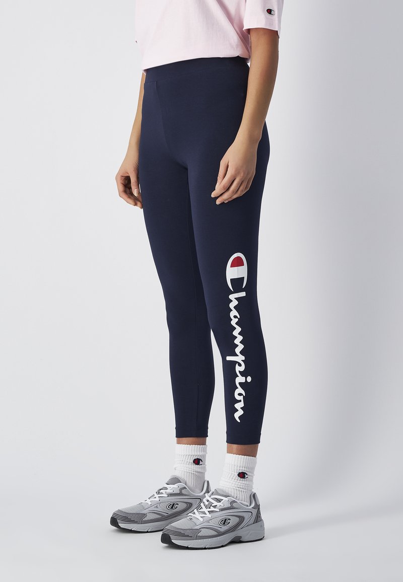 Granatowe legginsy z wysokim stanem, z białym logo "Champion" i małym czerwonym emblematem. Materiał ma gładką, elastyczną teksturę.