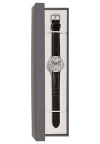 Montre en argent avec un cadran rond, bracelet en cuir noir à texture de crocodile, présentée dans une boîte grise avec un intérieur crème.