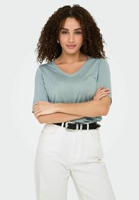 Camiseta de cuello en v de manga corta en azul claro, hecha de una tela suave, combinada con pantalones de mezclilla blancos de cintura alta y un cinturón negro con una hebilla plateada.